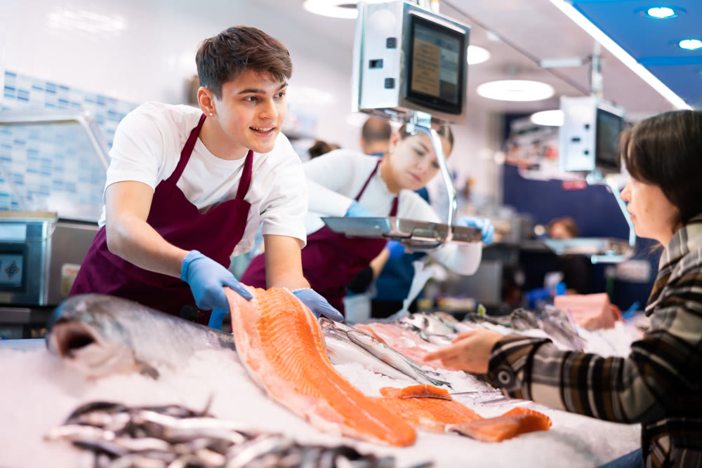 Portrait of man offering female customer fresh fish at seafood shop