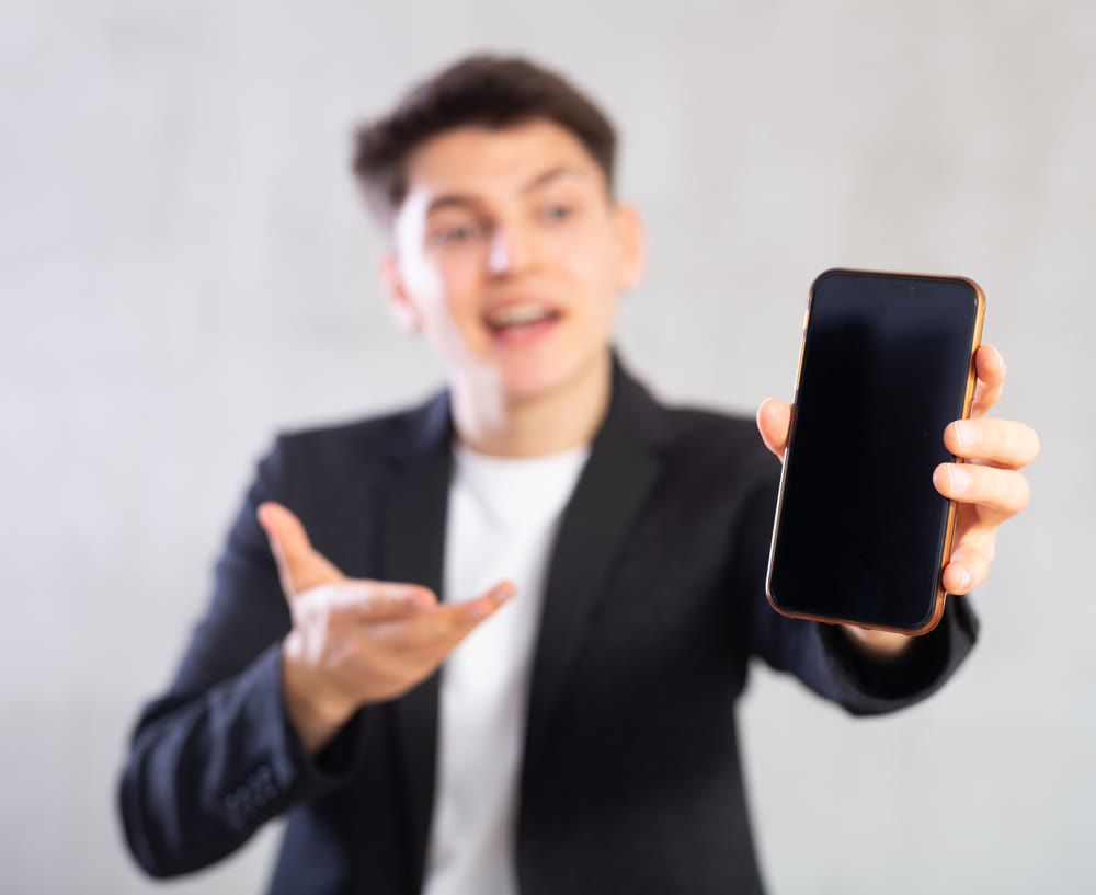 Smiling young guy holding mobile phone in his hand
