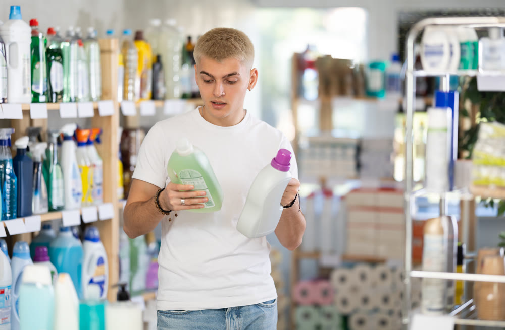Positive young man choosing liquid detergent at household goods in store