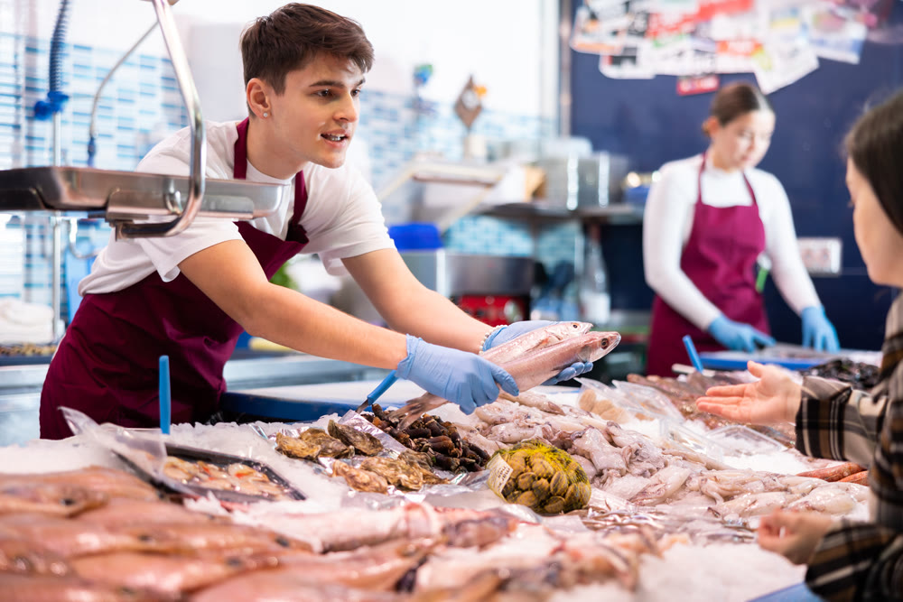 Positive salesman demonstrating red snapper to purchaser in fish store