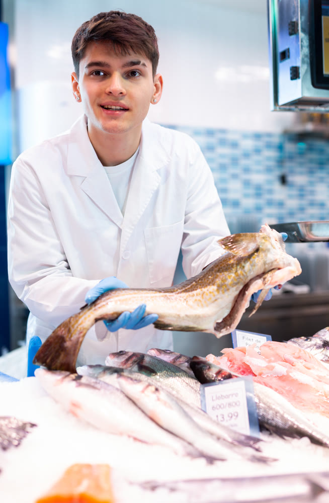Seller of fish department of a supermarket demonstrates fresh atlantic cod fish