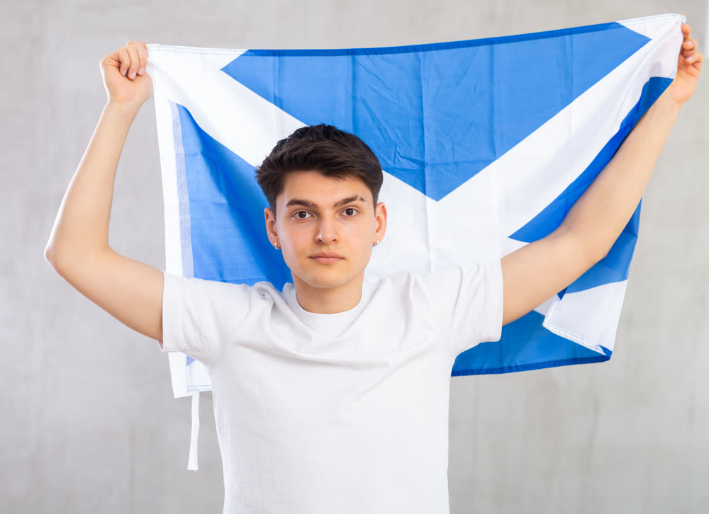 Focused young guy holding flag of Scotland