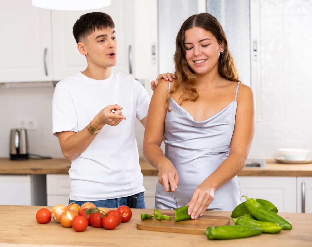Woman preparing vegetable salad and communicating with her husband in kitchen