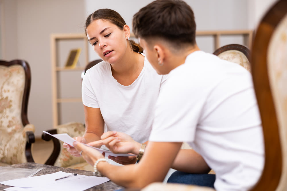 Young couple signing documents together while sitting on couch at home