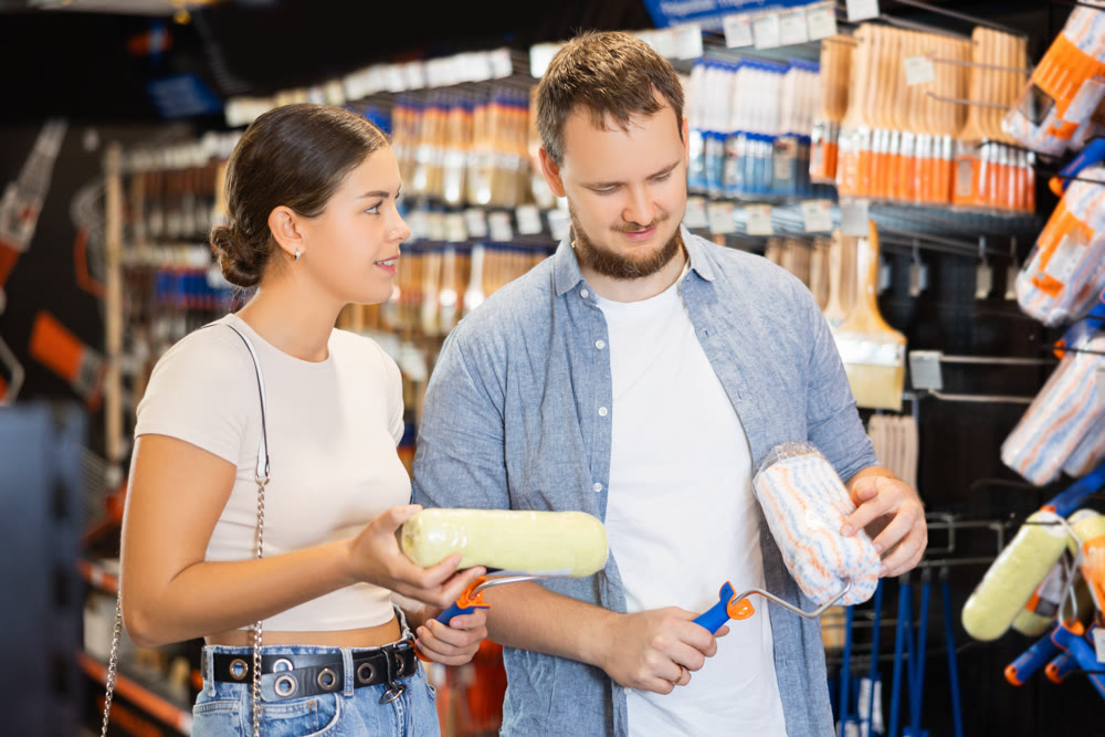 Married couple choose paint brush and paint roller together for their home renovation at hardware store