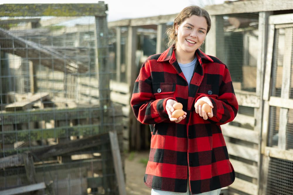 Young woman holding fresh eggs in chicken coop