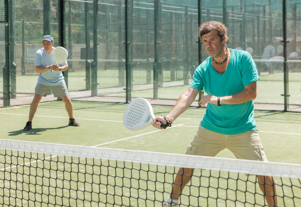 Men play padel on an outdoor tennis court. Hitting the ball with racket