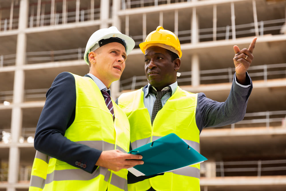 African-american engineer discussing a construction plan with a colleague shows him something