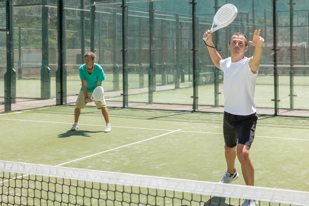 Young and adult men playing doubles padel