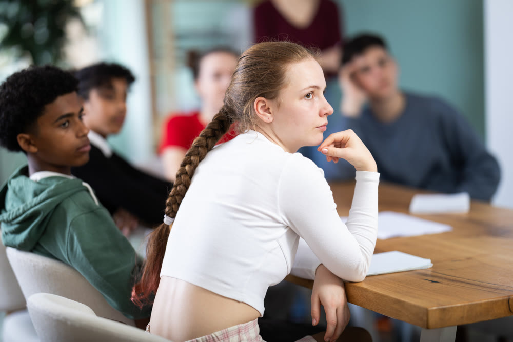 Schoolchildren teenagers sit at the table and carefully watch documentaries