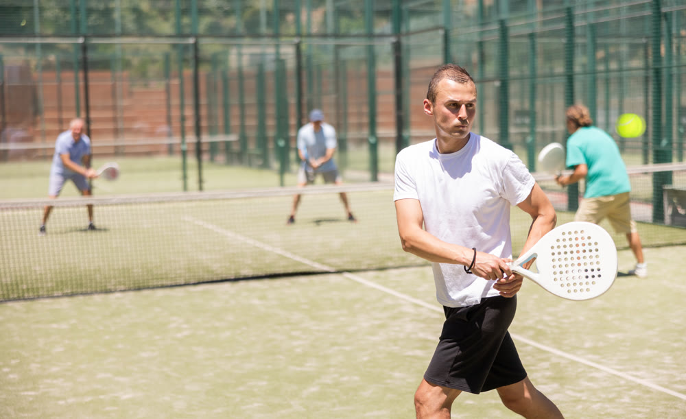 Adult and young men playing padel against two men