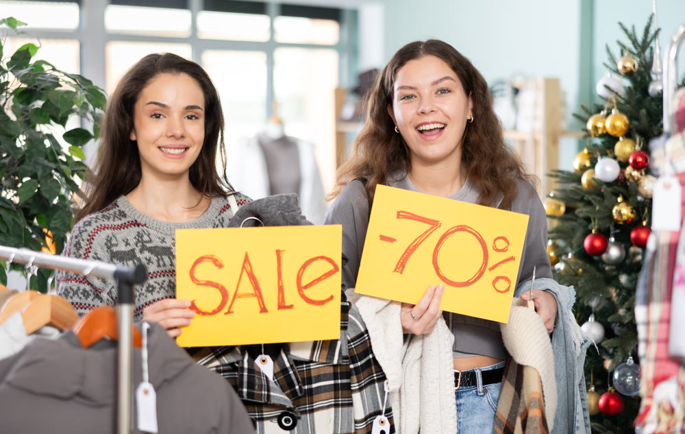 Two women holding posters of 70 percent discounts and sales in a clothing Christmas store