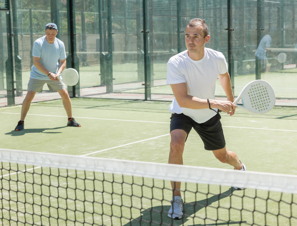 Young and adult men playing doubles padel