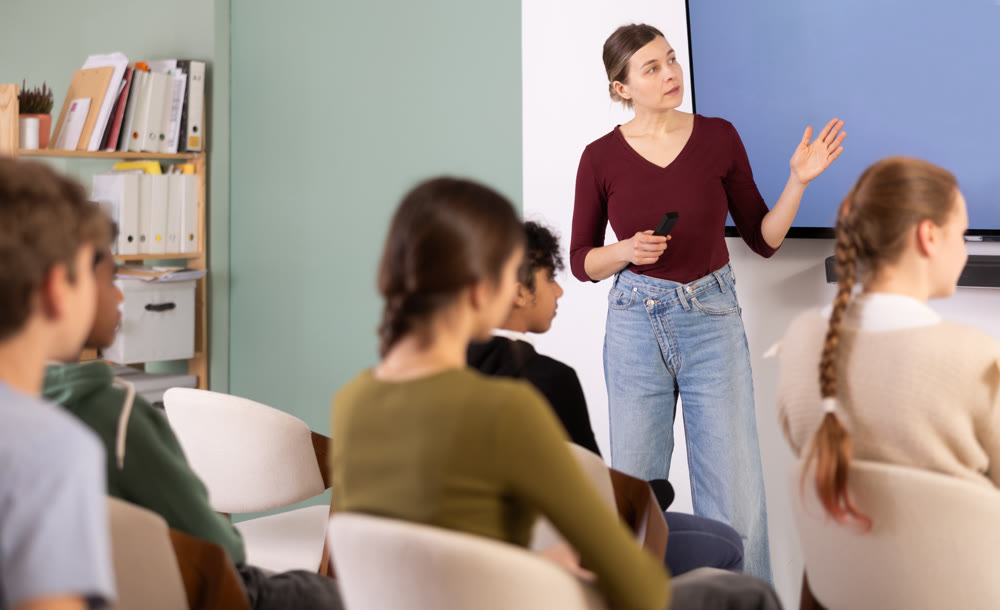 Teacher conducts a lesson in front of a group of students, explaining the material at the screen