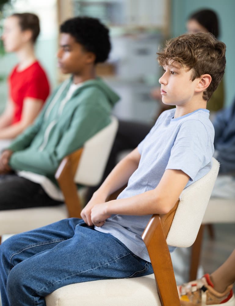 Teenage boy listening to teacher while sitting with classmates in classroom