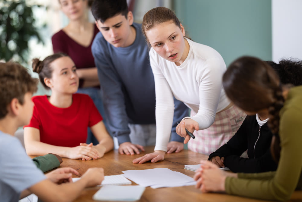 Group of teenagers and students discuss the task at the table in classroom