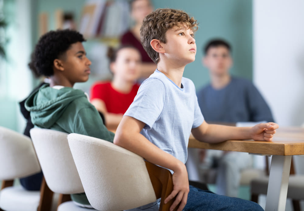 Teenage boy watching presentation while sitting with classmates in classroom