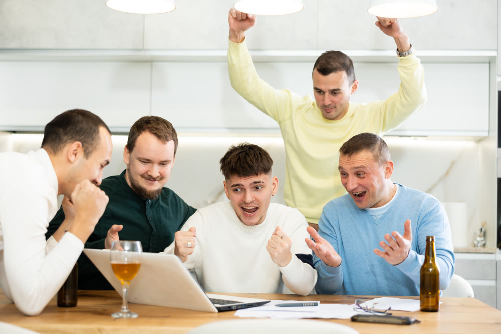 Group of football fans drinking beer and watching football match on laptop at home