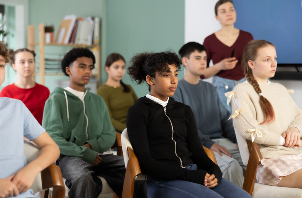 Teenage students listening to lecture while teacher stands in background
