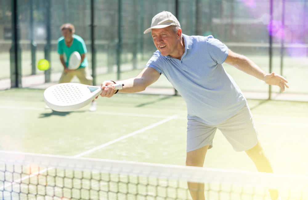 Portrait of sporty mature man playing padel on open court on autumn day, ready to hit ball. Health and active lifestyle concept