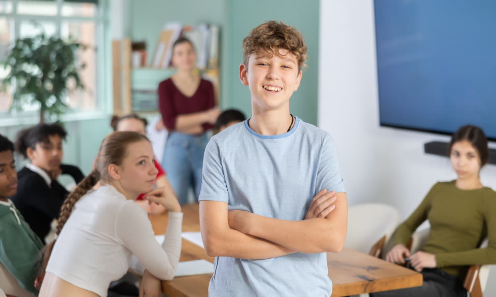Confident teenage boy standing with his back to classmates sitting at table