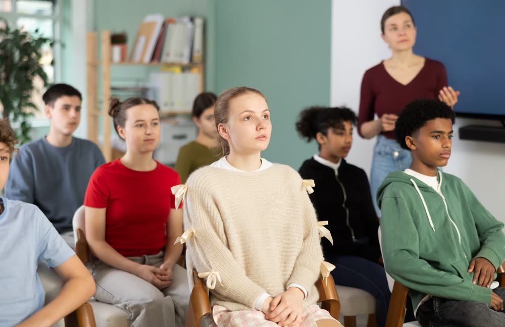 During meeting at class, teen pupil listen to lecture, female teacher in background.