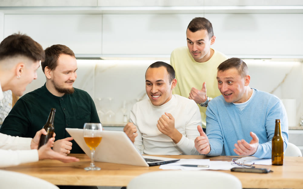 Group of football fans drinking beer and watching football match on laptop at home