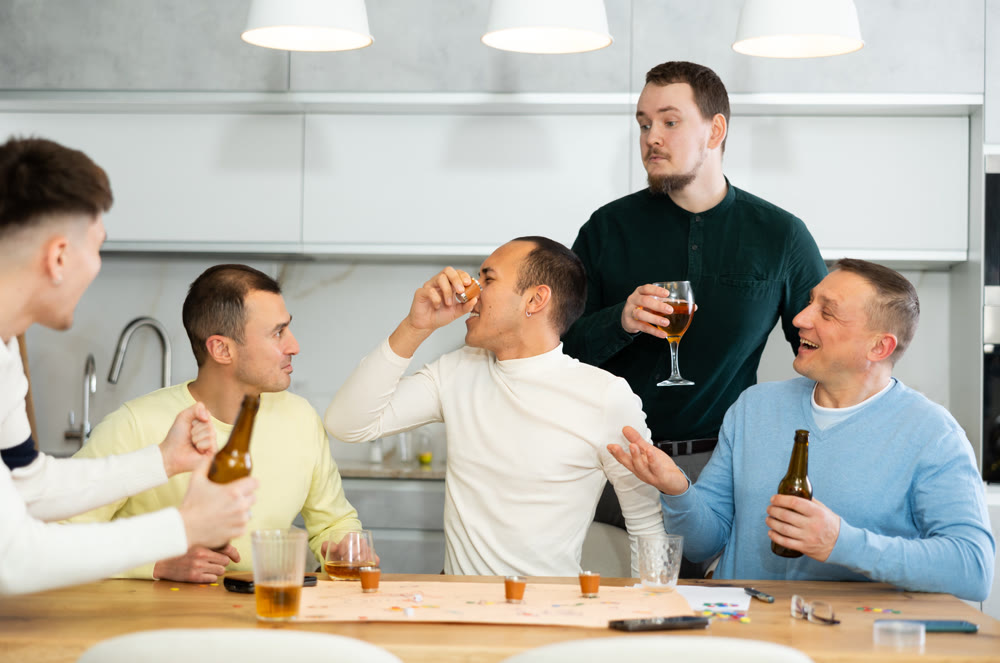 Defeated man taking shot while playing drinking board game with friends