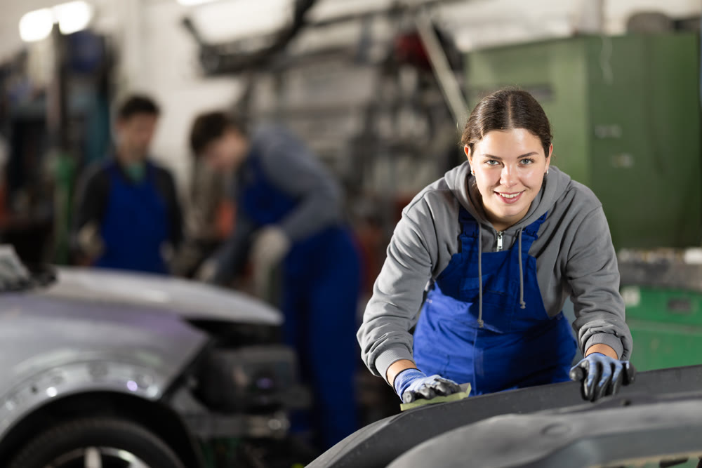 Woman car mechanic polishes car bumper - prepares bumper for painting in car service