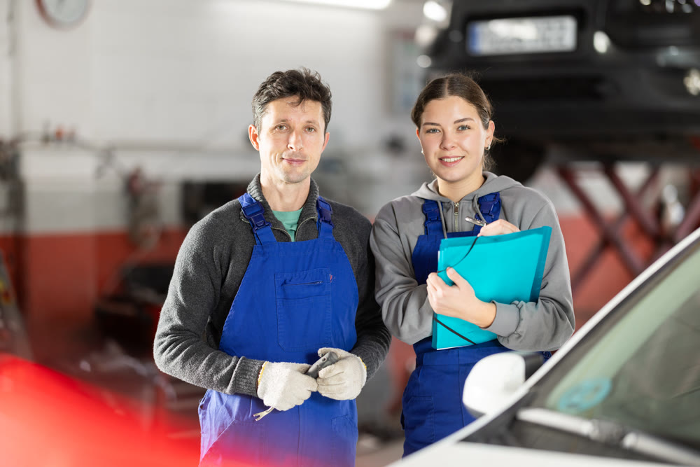 Young woman supervisor manager of car repair station with papers listens to male master