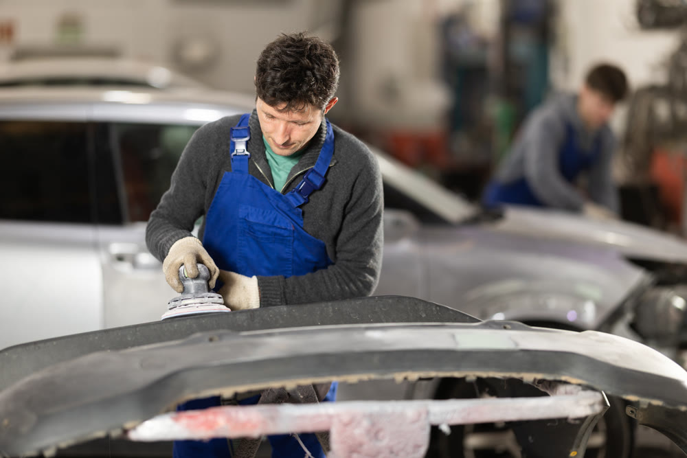 Car bumper repair in car service - professional car painter polishes and prepares bumper before painting