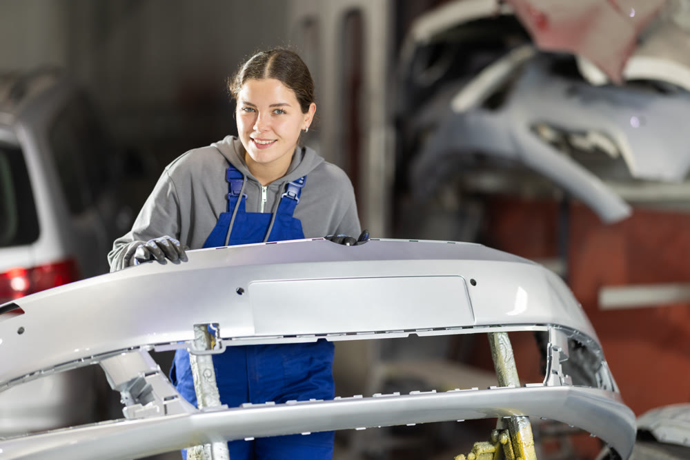 Female auto mechanic checks the quality of painting of a car bumper in car service