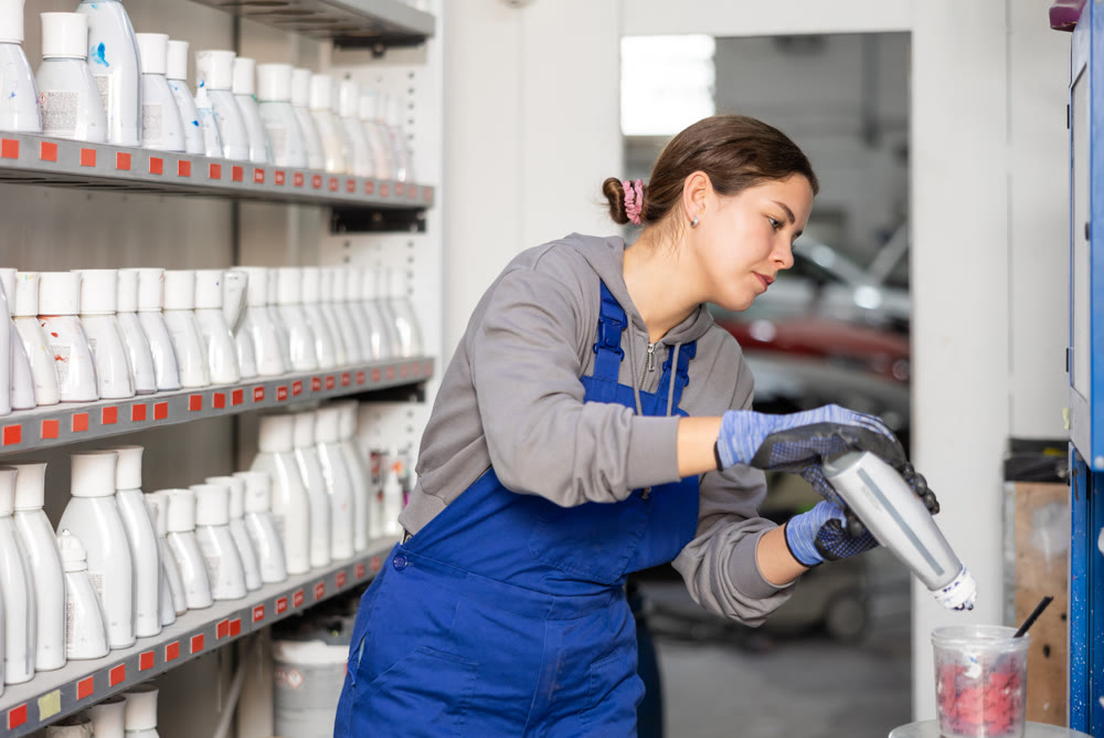 Girl colorist selects paint color by mixing different paint colors for subsequent painting of car in car service center