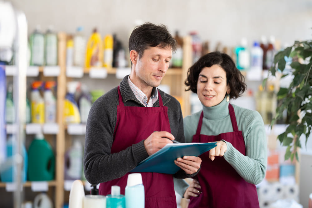 Couple employees, with paper and invoice in hands, make inventory in store.