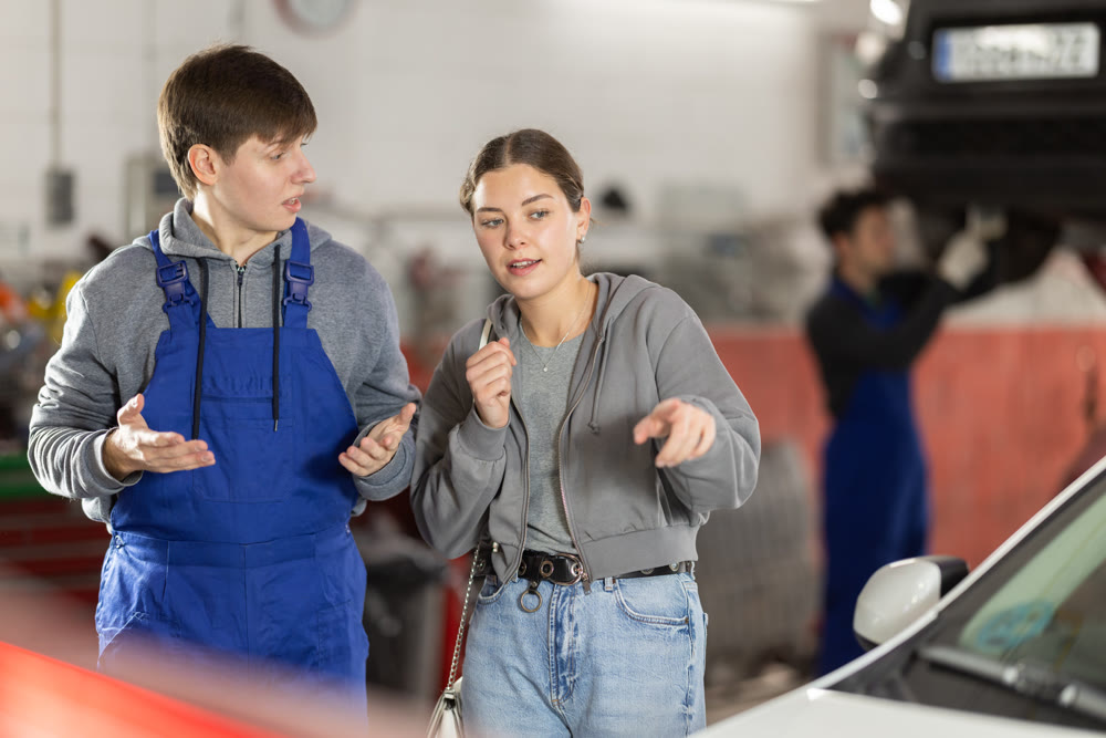 Male mechanic advises woman client on repairing of car in car service station
