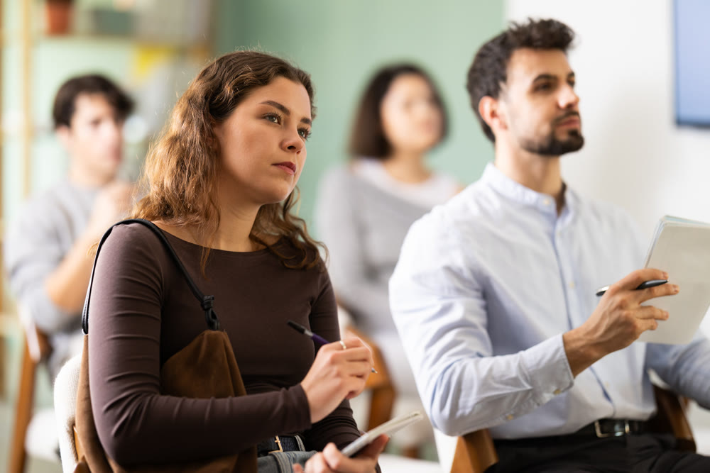 Woman listens attentively to teacher and takes notes in notebook during professional development course