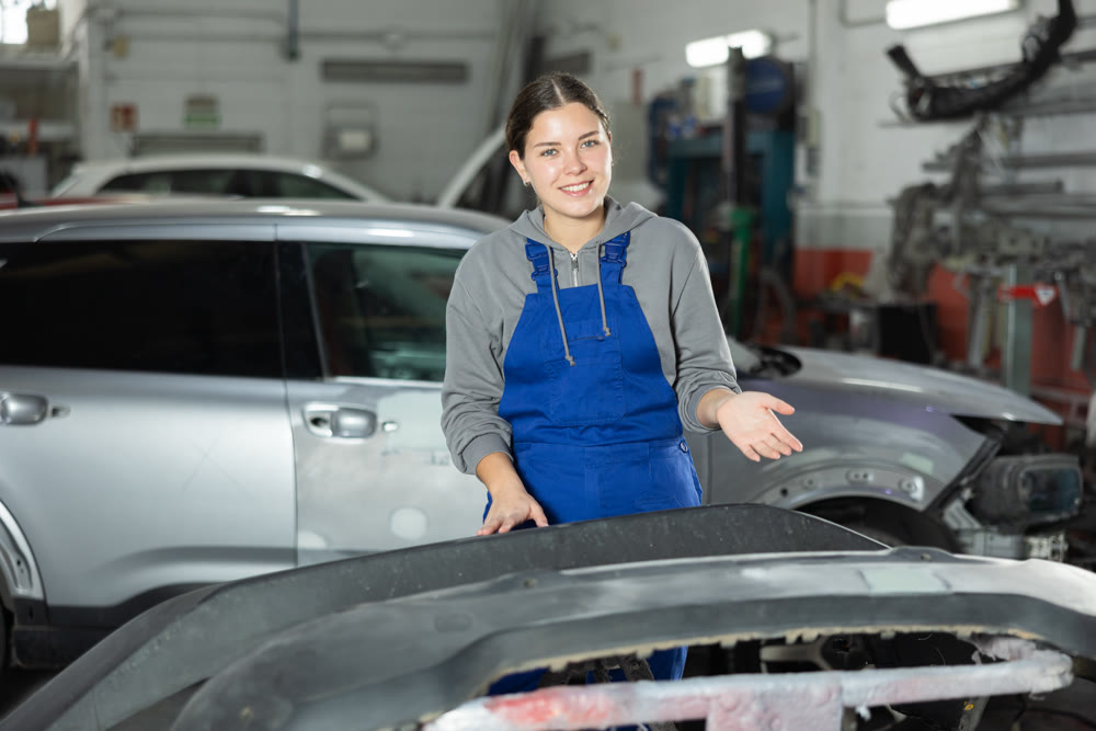 Young woman auto mechanic polishes body parts by car buffer polisher machine tool