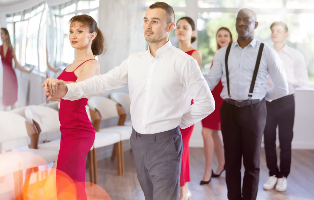 Confident man dancing waltz with female partner in red during group class