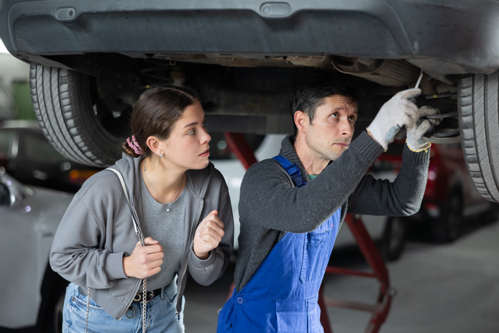 Girl watches as a professional mechanic repairs her car at car service center