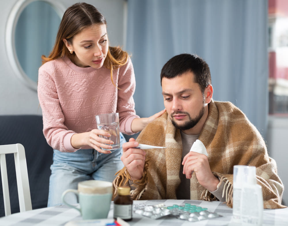 Woman giving glass of water to her ill husband at home