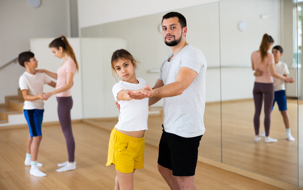 Teen girl learning to dance waltz in pair with father in studio