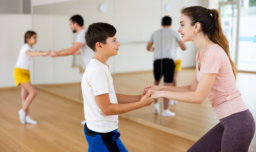 Young boy dancing waltz with his mother in gym