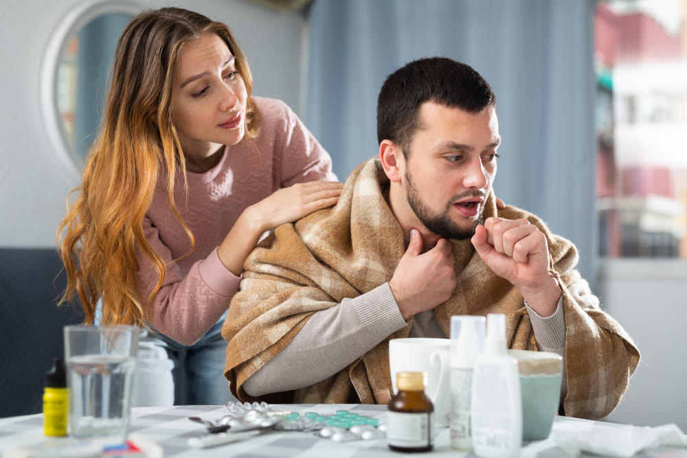 Man with cold symptoms sitting at home while girlfriend caring him