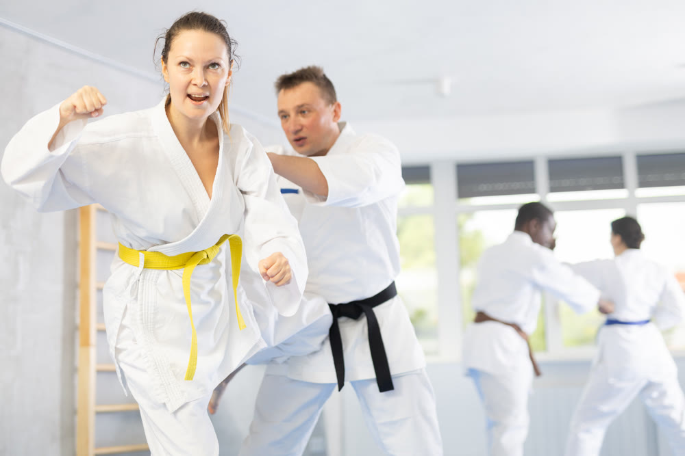 Middle-aged woman attendee of karate classes fighting with her opponent in sports hall
