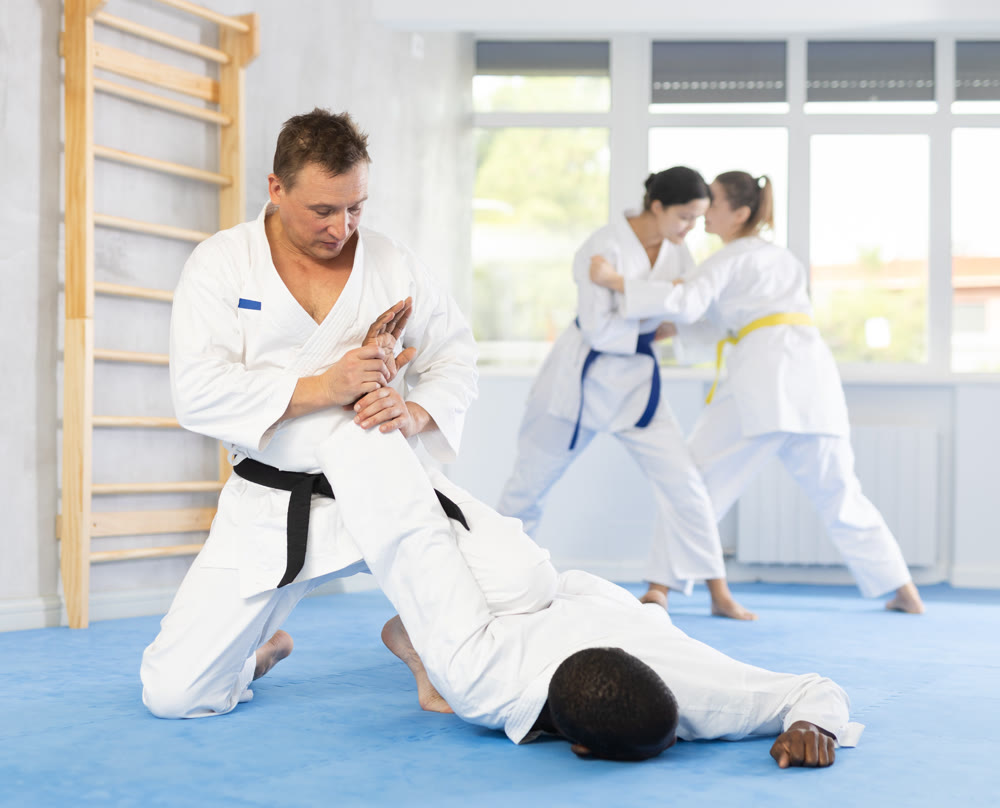 Judo or jiu-jitsu classes - two men practicing grabbing and throwing on sports mats under the guidance of trainer