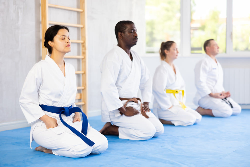 Group of multinational martial arts fighters in white kimonos sitting on knees on tatami