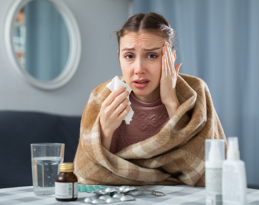 Sick woman with plaid on her shoulders suffers from runny nose