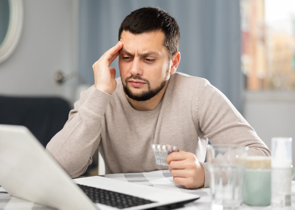 Man with pills in his hands is looking for diagnosis on the Internet using laptop