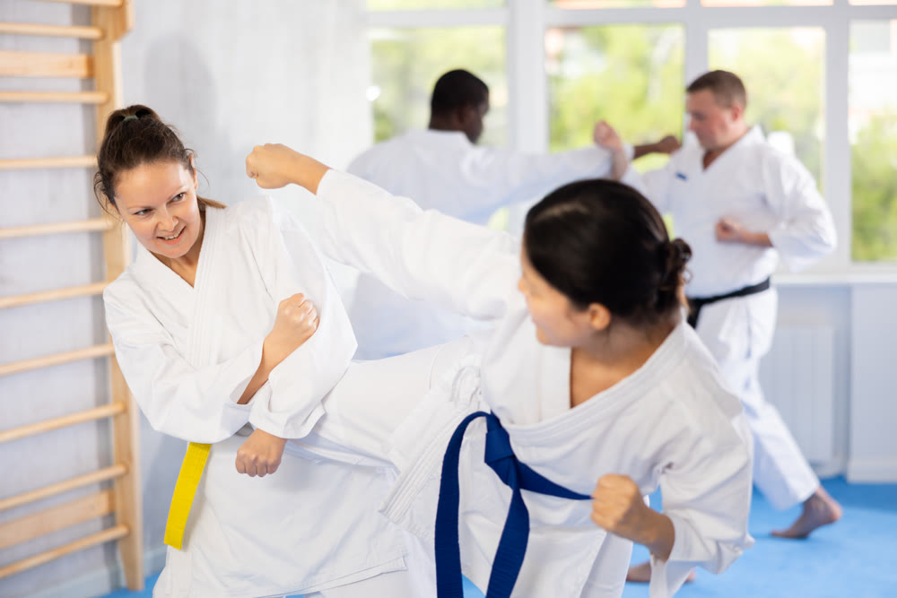 Karate with two female athletes practicing, training and sparring in fight class. Healthy, fit and active women in uniform learning self defense for safety