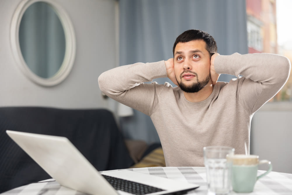 Man covering ears with hands because of loud noise in neighbors apartment